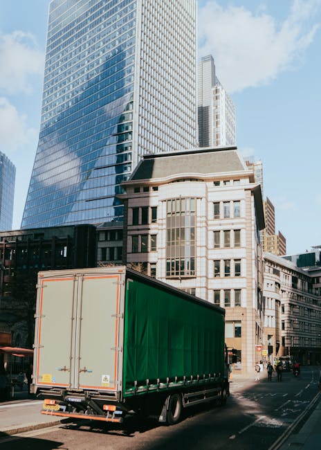 A white moving truck with its rear doors open is parked on the side of a city street in front of a building with a blue sign reading 'Dublin Mouldings' for house removals and furniture transport. Insi